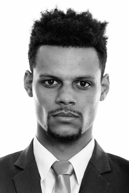 Foto de estudio de joven apuesto hombre de negocios africano con barba en traje aislado sobre fondo blanco en blanco y negro