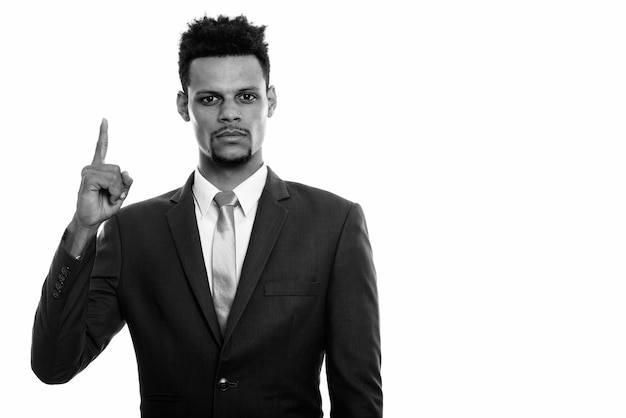 Foto de estudio de joven apuesto hombre de negocios africano con barba en traje aislado sobre fondo blanco en blanco y negro