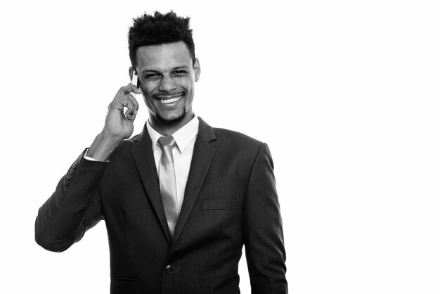 Foto de estudio de joven apuesto hombre de negocios africano con barba en traje aislado sobre fondo blanco en blanco y negro