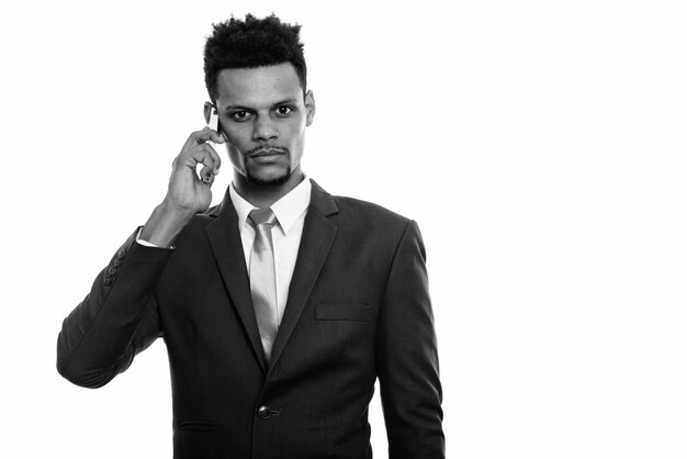 Foto de estudio de joven apuesto hombre de negocios africano con barba en traje aislado sobre fondo blanco en blanco y negro