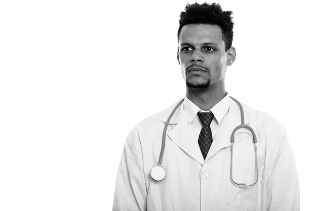 Foto de estudio de joven apuesto médico africano barbudo aislado sobre fondo blanco en blanco y negro