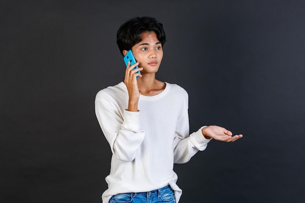 Foto de estudio del joven asiático LGBTQ gay glamour guapo bisexual homosexual modelo masculino en ropa casual de pie sonriendo sosteniendo el teléfono inteligente sobre fondo negro