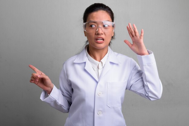 Foto de estudio de la joven y bella mujer asiática médico con gafas protectoras contra un blanco