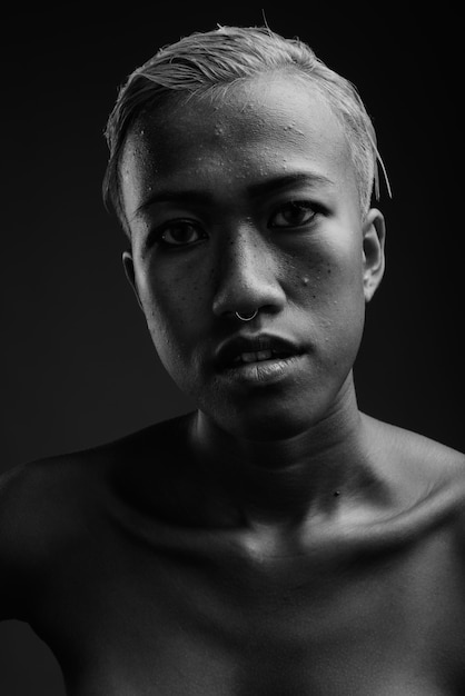 Foto de estudio de joven bella mujer rebelde con pelo corto contra gris en blanco y negro