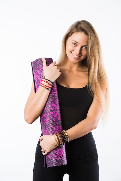 Foto de estudio de la joven y bella mujer rubia con estera de yoga y posando listo para el gimnasio