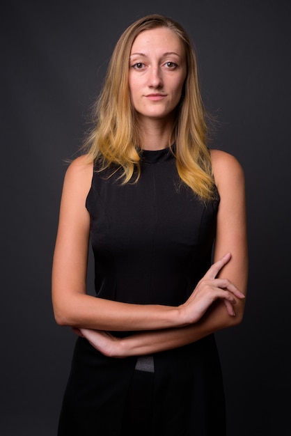 Foto de estudio de la joven empresaria hermosa con el pelo rubio recto contra gris