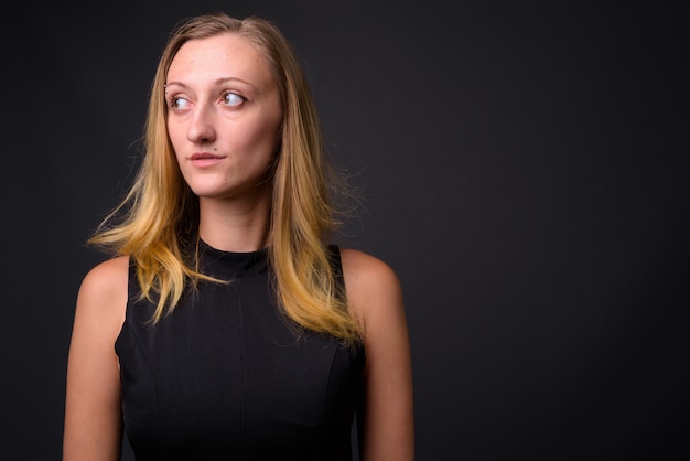 Foto de estudio de la joven empresaria hermosa con el pelo rubio recto contra gris