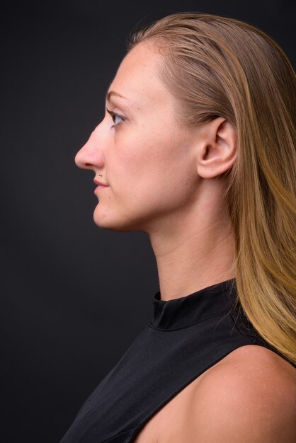 Foto de estudio de la joven empresaria hermosa con el pelo rubio recto contra gris