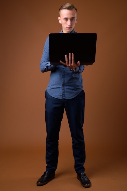 Foto de estudio de joven empresario guapo contra marrón