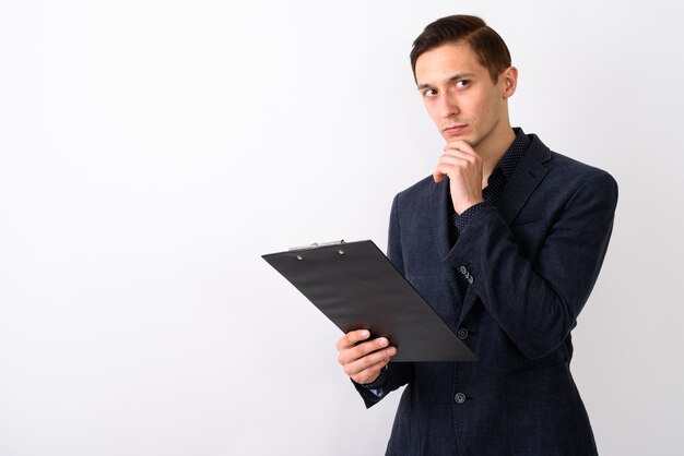 Foto de estudio de joven empresario guapo sosteniendo portapapeles mientras