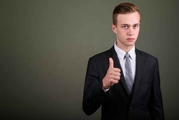 Foto de estudio de joven empresario guapo vistiendo traje con fondo de color