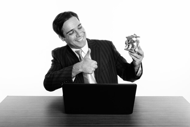 Foto de estudio del joven empresario persa sentado detrás de un escritorio de madera aislado, blanco y negro