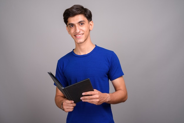 Foto de estudio de joven guapo adolescente persa contra un fondo gris