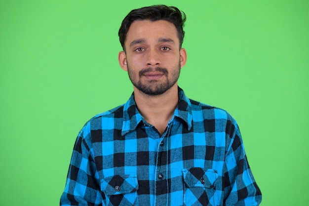 Foto de estudio de joven guapo hipster persa barbudo contra croma key con fondo verde