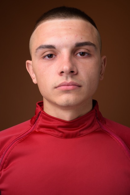 Foto de estudio de joven guapo con pelo corto contra marrón