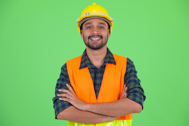 Foto de estudio de joven guapo persa barbudo trabajador de la construcción contra chroma key con fondo verde