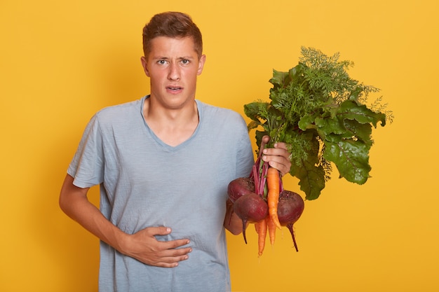 Foto de estudio de joven guapo con zanahorias y remolachas en la mano