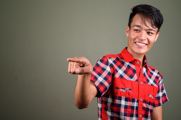 Foto de estudio de un joven indio adolescente hombre vestido con camisa a cuadros roja contra color