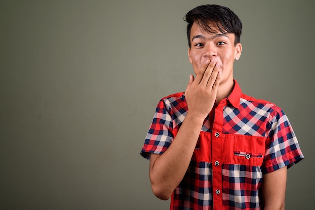 Foto de estudio de un joven indio adolescente hombre vestido con camisa a cuadros roja contra color