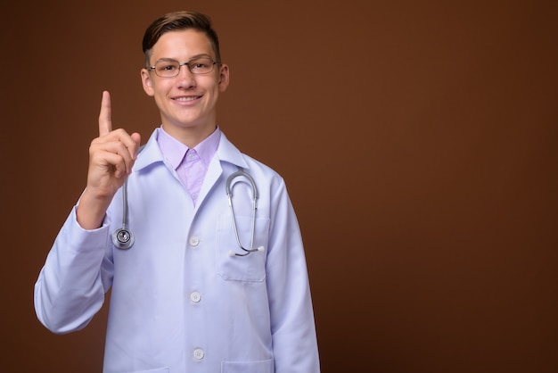 Foto de estudio de joven médico guapo contra el fondo marrón