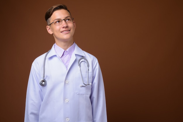 Foto de estudio de joven médico guapo contra el fondo marrón