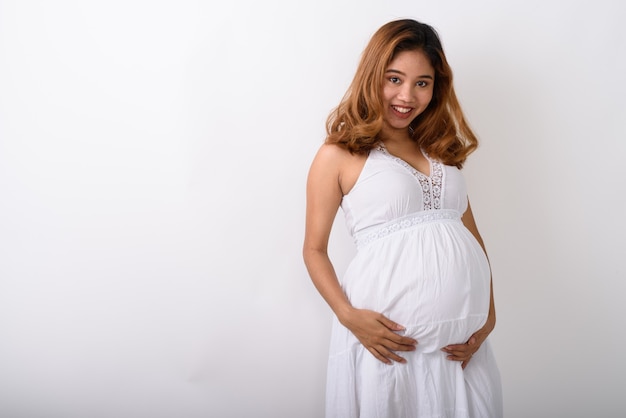 Foto de estudio de la joven mujer embarazada asiática feliz sonriendo contra