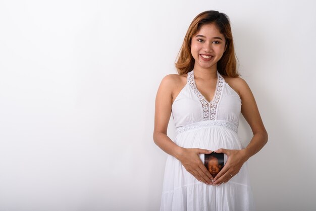 Foto de estudio de la joven mujer embarazada asiática feliz sonriendo mientras ho