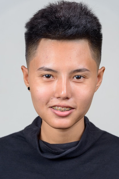 Foto de estudio de la joven mujer lesbiana asiática con pelo corto contra el fondo blanco.