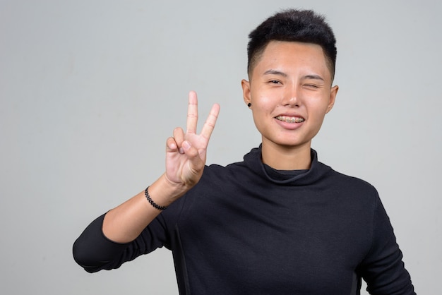 Foto de estudio de la joven mujer lesbiana asiática con pelo corto contra el fondo blanco.