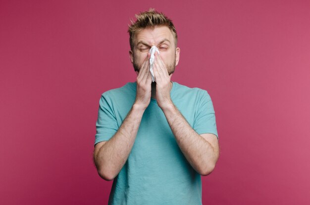 Foto de estudio de un joven con pañuelo. El enfermo tiene secreción nasal. el hombre hace una cura para el resfriado común