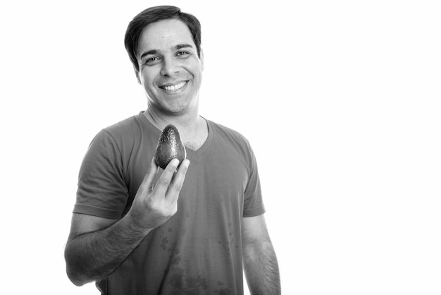 Foto de estudio de joven persa feliz sonriendo mientras sostiene aguacate aislado