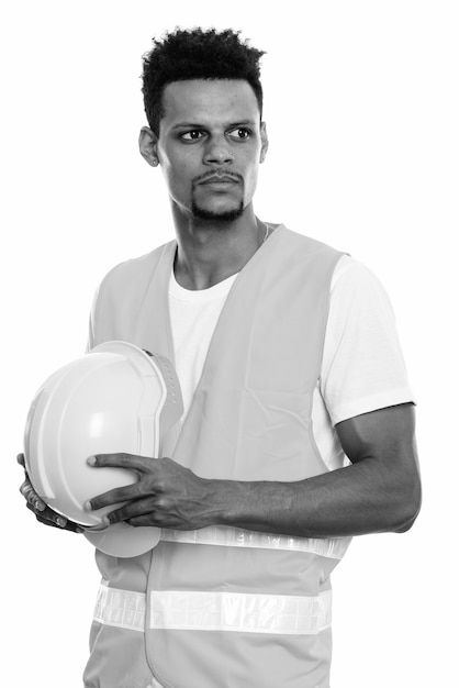 Foto de estudio de joven trabajador de la construcción africano barbudo aislado sobre fondo blanco en blanco y negro