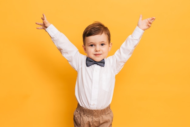 Una foto de estudio de un lindo niño haciendo muecas se encuentra sobre un fondo amarillo. Niño gracioso