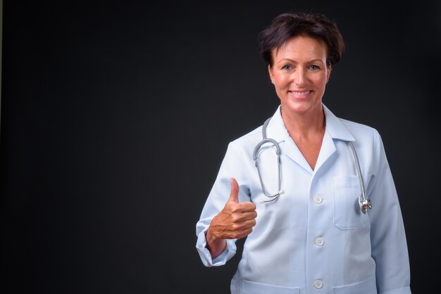 Foto de estudio de madura hermosa doctora escandinava con pelo corto sobre fondo negro