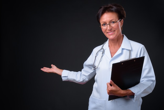 Foto de estudio de madura hermosa doctora escandinava con pelo corto sobre fondo negro