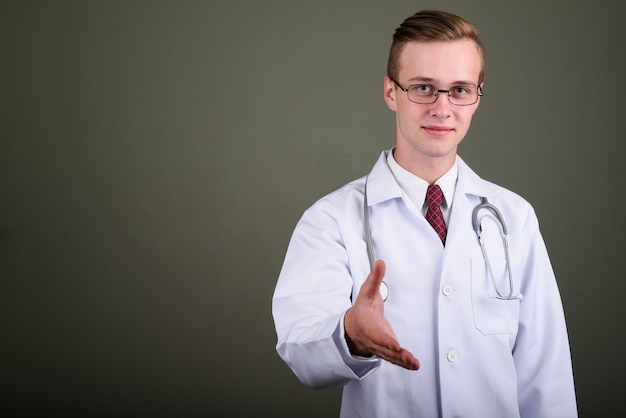 Foto de estudio de médico joven guapo con anteojos contra el fondo de color