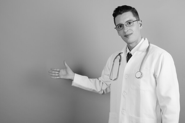 Foto de estudio de médico joven guapo con anteojos contra un fondo gris en blanco y negro