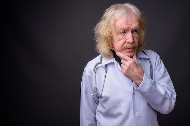 Foto de estudio de médico senior con bigote contra un fondo gris