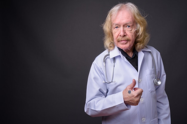 Foto de estudio de médico senior con bigote contra un fondo gris