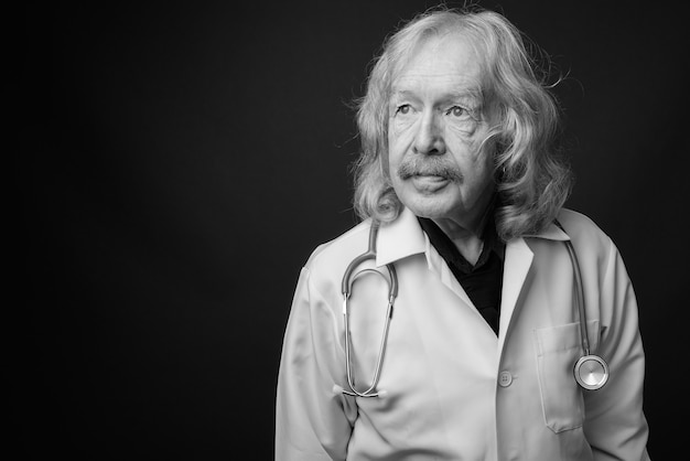 Foto de estudio de médico senior con bigote contra la pared gris