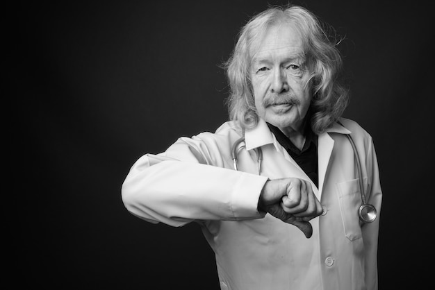 Foto de estudio de médico senior con bigote contra la pared gris