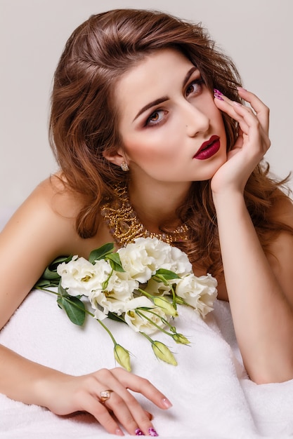 Foto de estudio de moda de hermosa mujer morena con maquillaje brillante con un ramo de eustoma púrpura y blanco