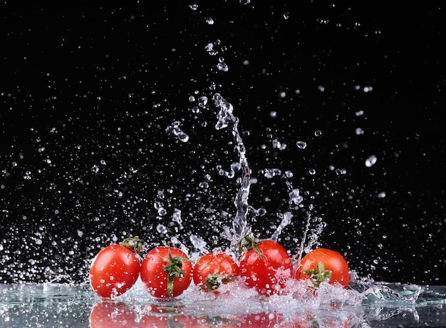 Foto de estudio con movimiento de congelación de tomates cherry en salpicaduras de agua sobre fondo negro