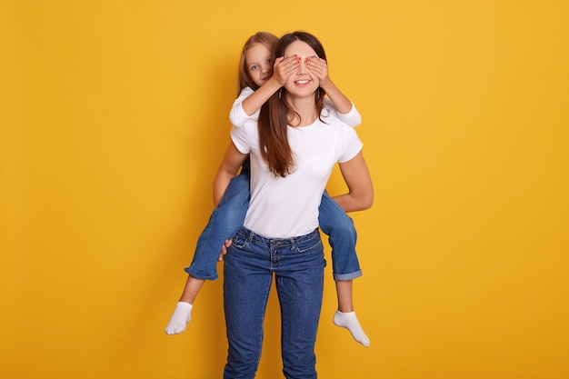 Foto de estudio de mujer dando pyggyback ride indoor, mujer vistiendo camiseta casual blanca y jeans