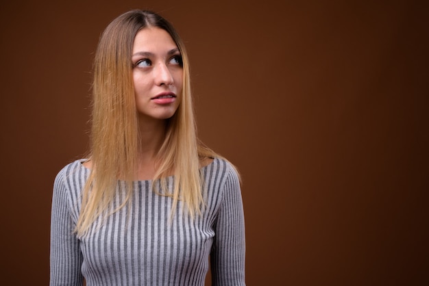 Foto de estudio de mujer hermosa joven pensando contra la pared marrón