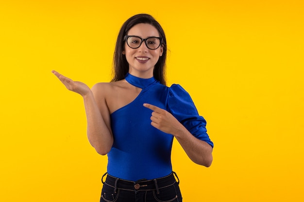 Foto de estudio de mujer joven con gafas con blusa azul sobre fondo amarillo con expresión facial