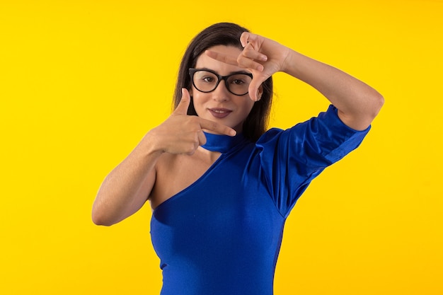 Foto de estudio de mujer joven con gafas con blusa azul sobre fondo amarillo con varios expr faciales