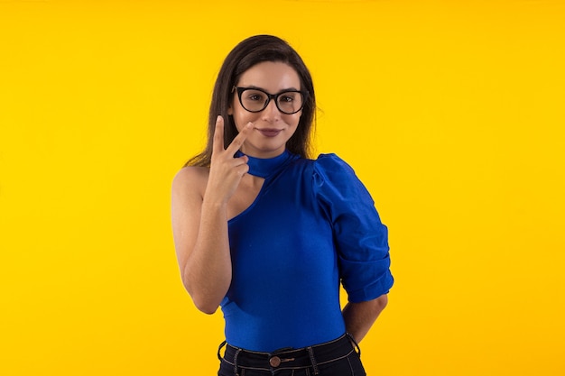 Foto de estudio de mujer joven con gafas con blusa azul sobre fondo amarillo con varios expr faciales