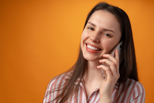 Foto de estudio de mujer joven hablando por teléfono contra la superficie amarilla