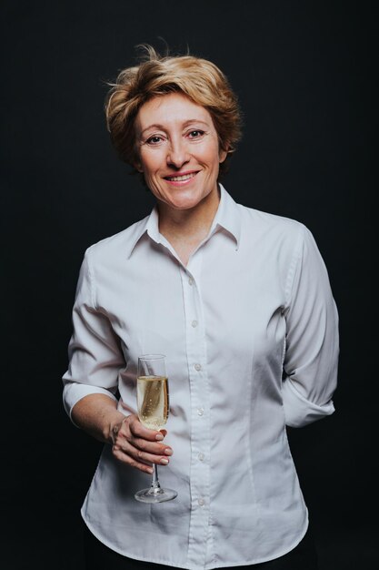Una foto de estudio de una mujer de mediana edad con ropa informal posando con una copa de champán aislada en negro